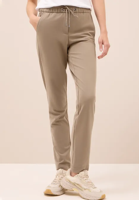 Beige Jogginghose mit Kordelzug, weiße Sneakers, weiße Oberteil.